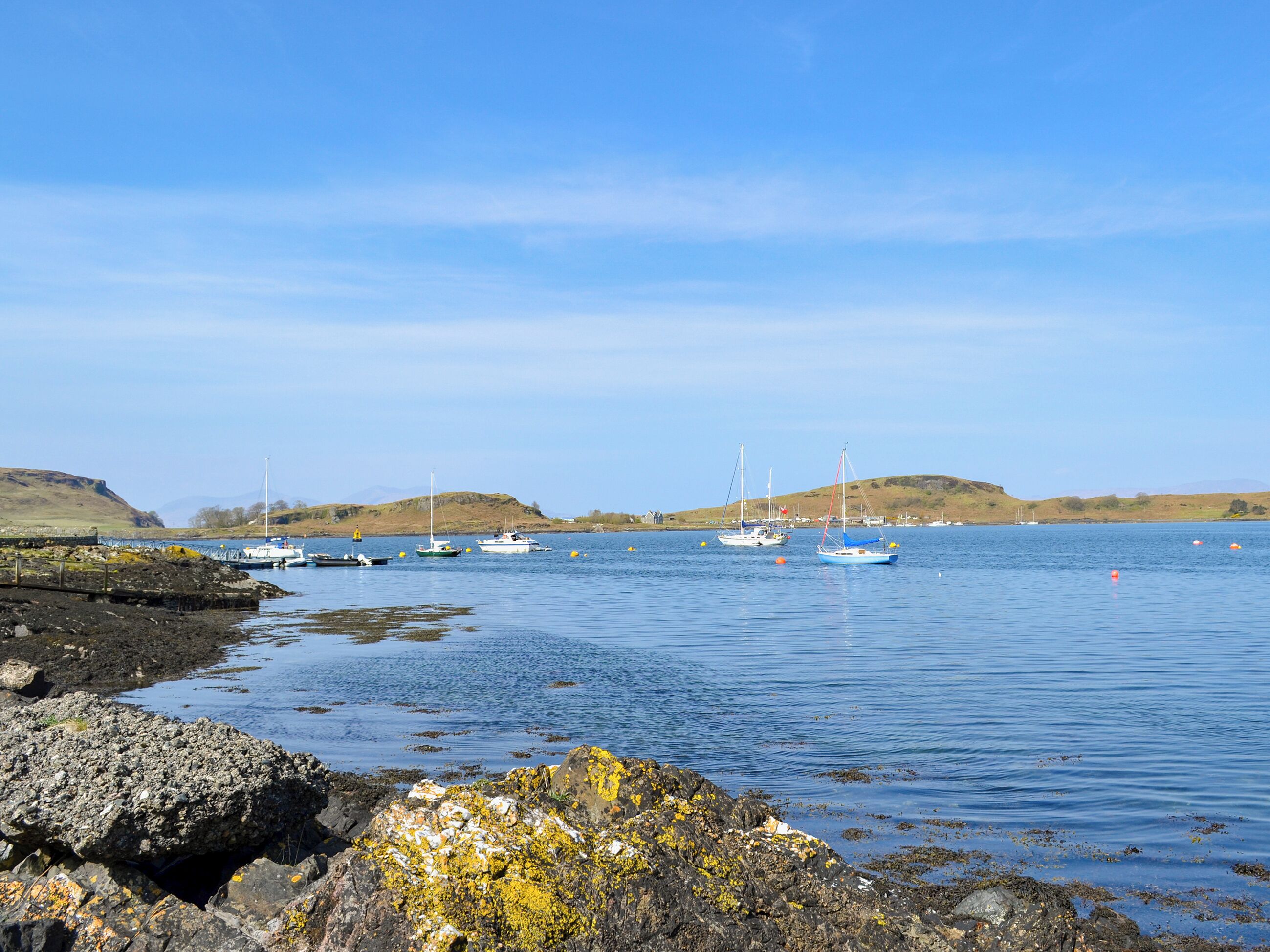A coastal scene with boats, rocky shore, and hills in the background.