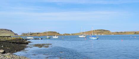 A coastal scene with boats, rocky shore, and hills in the background.
