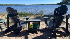 Two Adirondack chairs facing a lake with a small table and a bucket between them.