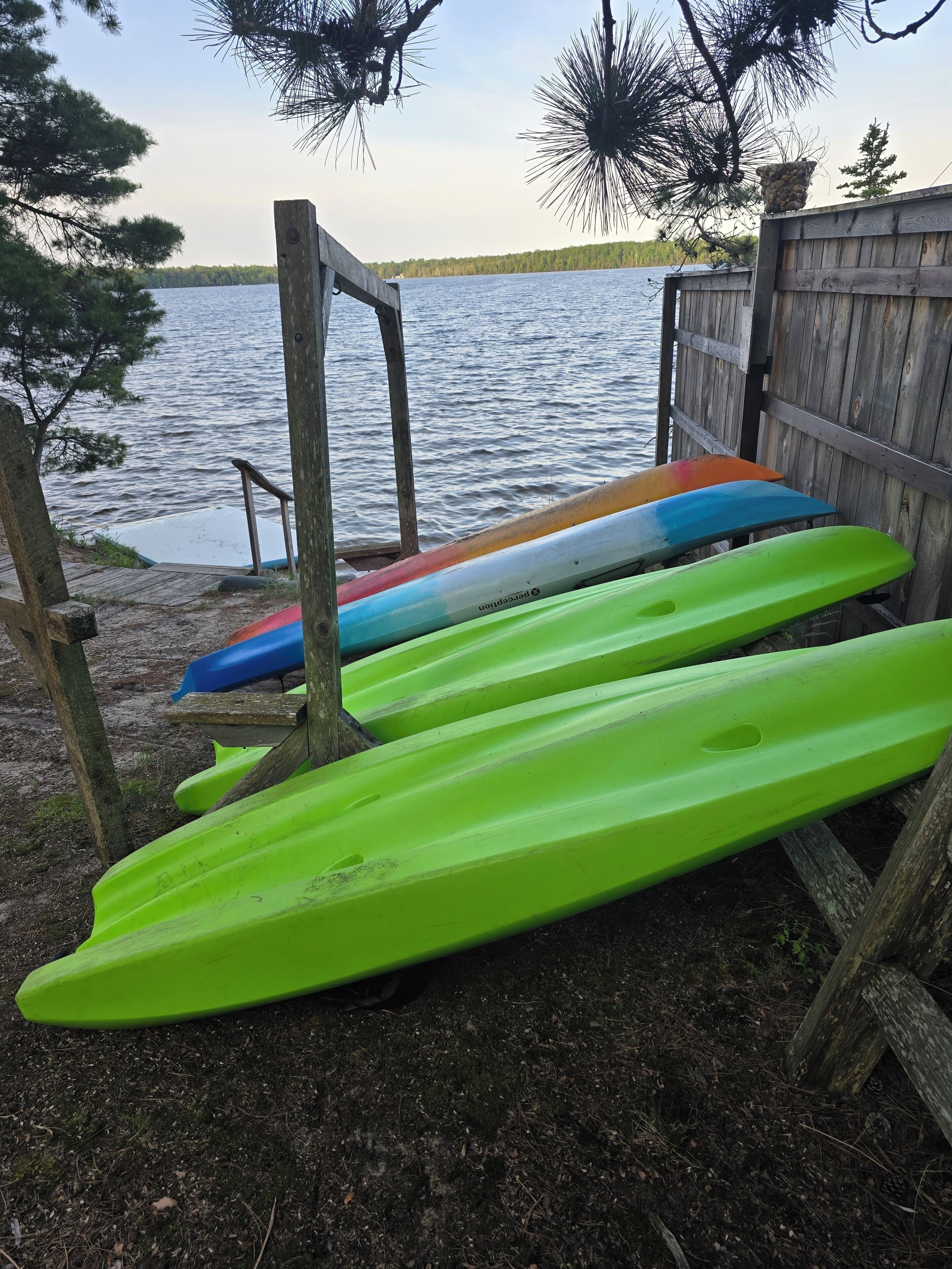 A dock with kayaks and a wooden fence by a lake.