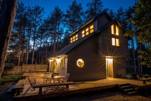 A wooden cabin with a deck, multiple windows, and a circular light fixture.