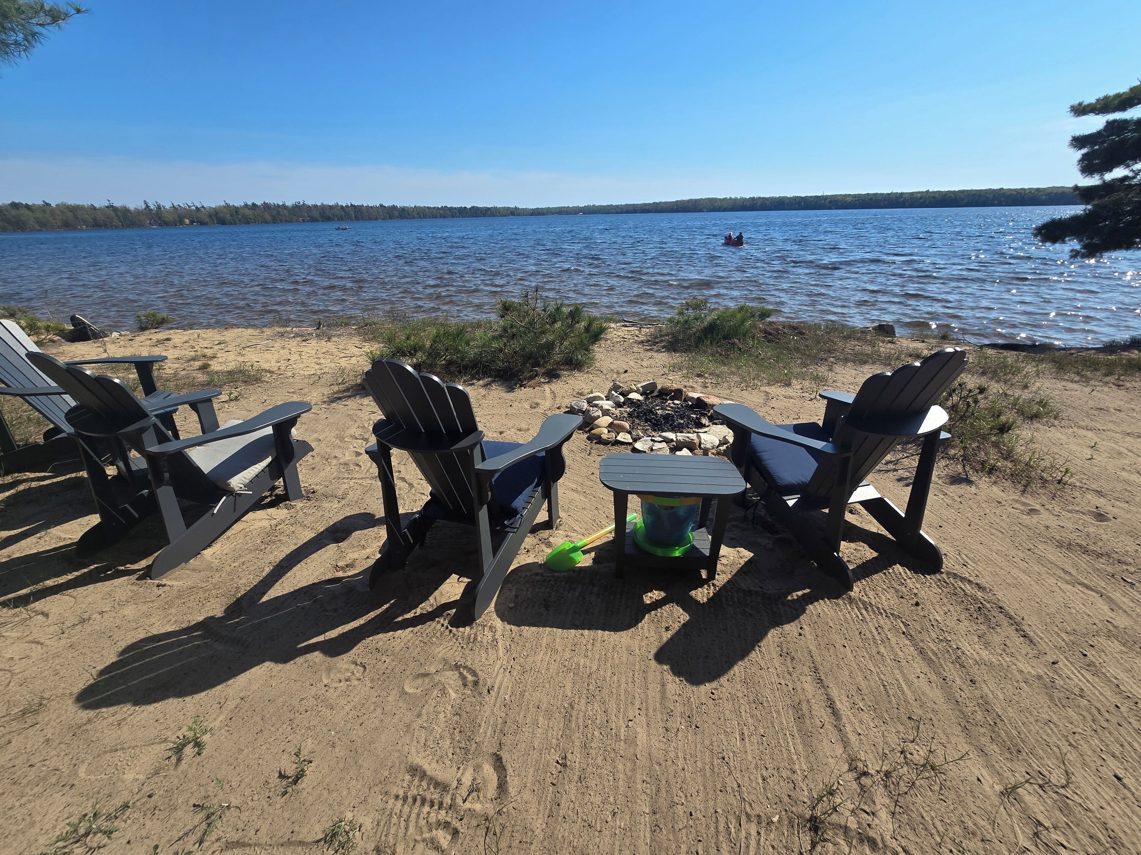 En vacker plats vid sjön med Adirondack-stolar, en eldstad och utsikt över vattnet.