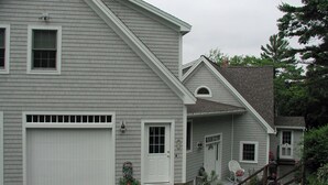 A two-story house with a garage, a front porch with a rocking chair, and a small garden area with gravel and plants.