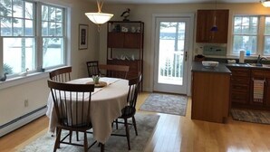 A kitchen with a dining table, chairs, a chandelier, wooden cabinets, and a view through the door.