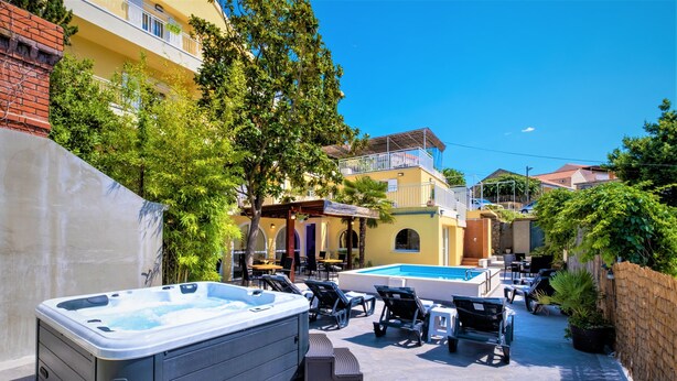 A hot tub and outdoor seating area with a pool, surrounded by buildings and greenery. - Castelletto - Deluxe Double Room with Sea View and Airport Transfer (Cavtat)
