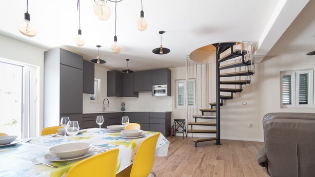 A modern kitchen with dark cabinets, a central island with yellow chairs, and a spiral staircase. - Villa Lali - Modern Villa near the sea in Lukoran (Lukoran)