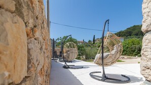 A stone wall, outdoor seating area with wicker chairs, and a clear view of a hillside with houses. - Villa Lali - Modern Villa near the sea in Lukoran (Lukoran)