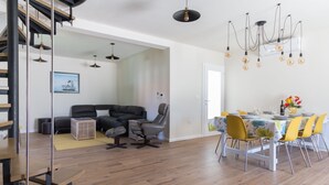 A modern living room with a sofa, chairs, a dining table with yellow chairs, and a staircase with a metal railing. - Villa Lali - Modern Villa near the sea in Lukoran (Lukoran)