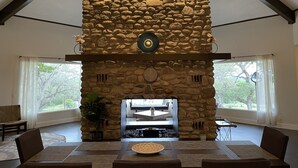 Lareira de pedra com design moderno, rodeada por uma área de jantar com uma mesa grande e cadeiras.