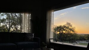 Sala de estar com uma grande janela, um sofá, uma mesa de centro e vista para árvores e colinas.