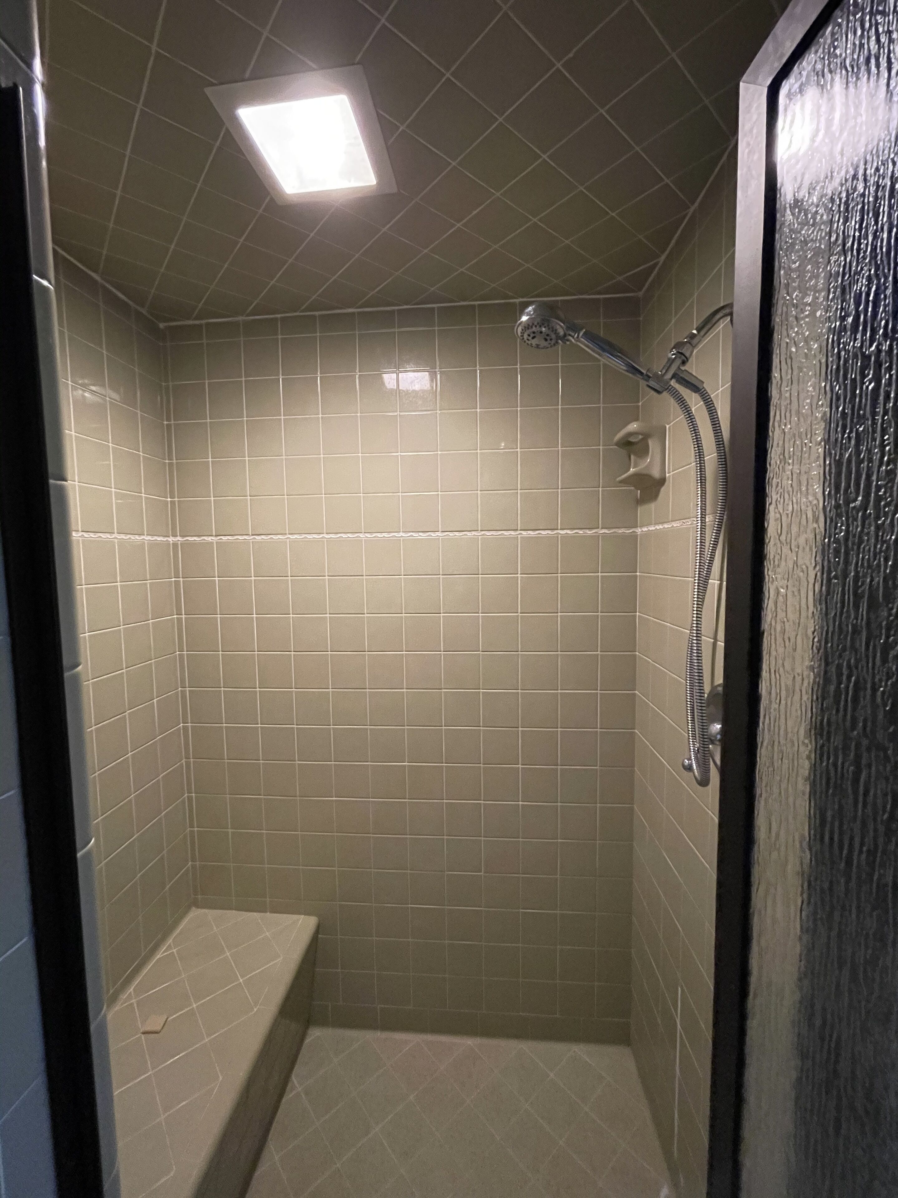 Pequeño baño con azulejos, banco y ducha de mano.