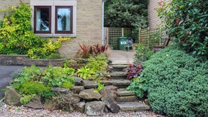 Ein Garten mit einem Kiesweg, der zu einem hölzernen Tor führt, umgeben von verschiedenen Pflanzen und Sträuchern.
