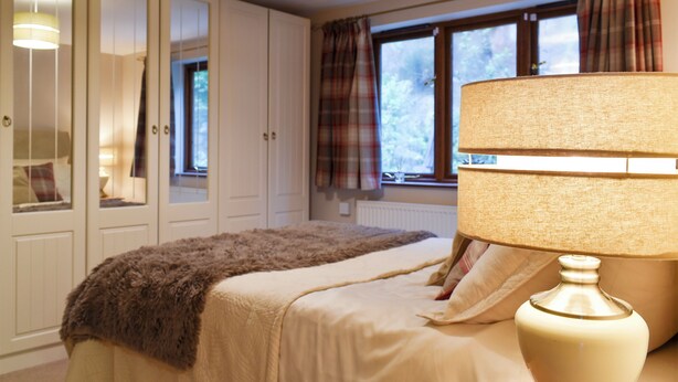 Ein Schlafzimmer mit einem Bett, einer Nachttischlampe, einem Fenster mit Vorhängen und einem Kleiderschrank.