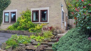 Ein Steinhaus mit Ziegelverkleidung, großen Fenstern und einem gepflegten Garten mit verschiedenen Pflanzen und einem Steingarten.