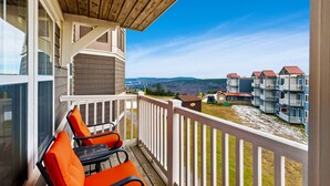 Ein Balkon mit zwei orangenen Stühlen und einem Tisch, der einen Blick auf eine Wohngegend mit mehreren Gebäuden und hügelige Fernlandschaft bietet.