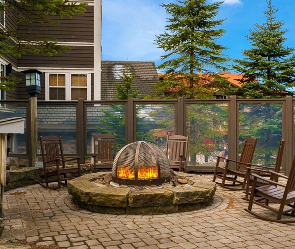 A stone fire pit with a metal grill in the center, surrounded by wooden chairs. - 1BR Allegheny Springs | No Resort Fee | Ski-In/Out | Sleeps 4 (Snowshoe)