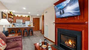 Ein Wohnzimmer mit Kamin, einem darüber montierten Fernseher und einer Küche im Hintergrund.