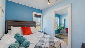 Une chambre avec un grand lit, une table de chevet, une fenêtre avec des stores et une vue sur l’extérieur.