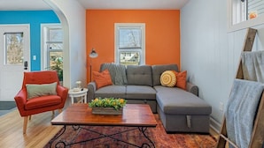 Un salon avec un canapé d’angle gris, un fauteuil rouge, une table basse en bois et un tapis à motifs.