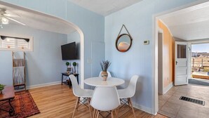 Un coin repas avec une table ronde, des chaises blanches, un ventilateur de plafond et un téléviseur fixé au mur.