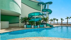 A swimming pool with a water slide and palm trees.