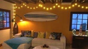 A cozy living room with a sofa, a coffee table, and a surfboard decoration on the wall. - Villa familiale dans grand jardin arboré à 200 m de la plage et proche village.. (Saint-Gildas-de-Rhuys)