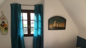 A bedroom with a bed, teal curtains, a window, a wall clock, and a tropical-themed decoration. - Villa familiale dans grand jardin arboré à 200 m de la plage et proche village.. (Saint-Gildas-de-Rhuys)