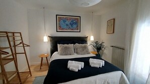 A neatly arranged hotel room with a bed, two bedside tables, a hanging light fixture, a framed picture on the wall, and a window with curtains. - Gîte T2 Aspres (Tautavel)