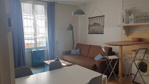A living room with a sofa, a dining table, and a washing machine. - Gîte T2 Aspres (Tautavel)
