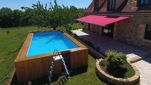 A swimming pool with a wooden deck, a stone house with a red awning, and a well-maintained lawn. - La Grange 🌿 (Le Bugue)
