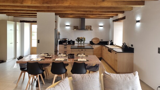 A modern kitchen with wooden cabinetry, a central island, and a dining area with a table set for four. - La Grange 🌿 (Le Bugue)
