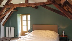 A bedroom with a large bed, wooden beams, a radiator, and a window. - La Grange 🌿 (Le Bugue)