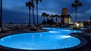 A swimming pool with a curved design, surrounded by palm trees and a fence. - 2 bedroom, gulf facing master en suite.  Includes 2 seasonal beach chairs. (Panama City Beach)