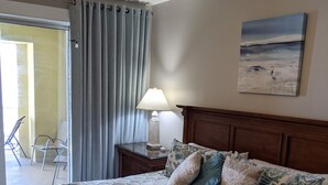 A hotel room with a bed, a ceiling fan, a lamp, and a painting on the wall. - 2 bedroom, gulf facing master en suite.  Includes 2 seasonal beach chairs. (Panama City Beach)