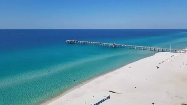 A beach with a long pier extending into the ocean, a sandy shore, and clear blue water. - 2 bedroom, gulf facing master en suite.  Includes 2 seasonal beach chairs. (Panama City Beach)