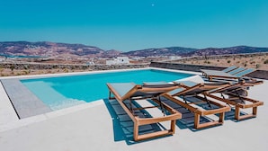 A rooftop pool with clear blue water, surrounded by wooden lounge chairs and a view of distant mountains. - Two Bedroom Suite  with Private Pool (Mykonos)
