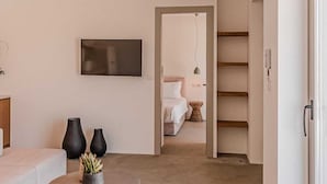 A modern living room with a sofa, a round table with a plant, and a flat-screen TV on the wall. - Two Bedroom Suite  with Private Pool (Mykonos)