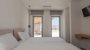 A bedroom with a bed, a TV mounted on the wall, and a balcony with a stone wall and a view of the landscape. - Two Bedroom Suite  with Private Pool (Mykonos)