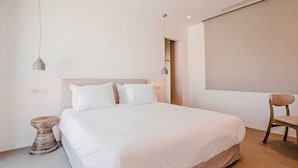 A bedroom with a large bed, two bedside lamps, a chair, and a window with a blind. - Two Bedroom Suite  with Private Pool (Mykonos)