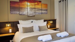 A hotel room with a large bed, a headboard with built-in lighting, a wall-mounted artwork of a sunset over the ocean, and a window with curtains. - Villa Cosy, Pool, Spa, Relaxation Area (Sauna & Hammam) 8 km from the beaches! (Pordic)