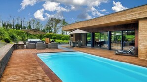 A modern outdoor pool area with wooden decking, lounge chairs, and a barbecue setup. - Villa Cosy, Pool, Spa, Relaxation Area (Sauna & Hammam) 8 km from the beaches! (Pordic)