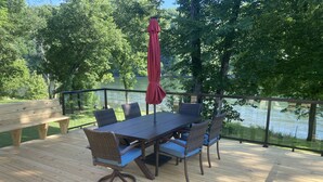 Terraza de madera con una mesa y sillas, con vista a un cuerpo de agua.