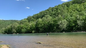 Un lago sereno con una persona de pie en el centro, rodeado por una ladera boscosa.