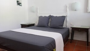 A bedroom with a bed, two bedside tables, a nightstand, a wall-mounted lamp, and a small table with a lamp.