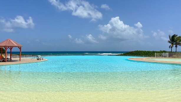 A clear blue sky, a swimming pool, and a beach view.