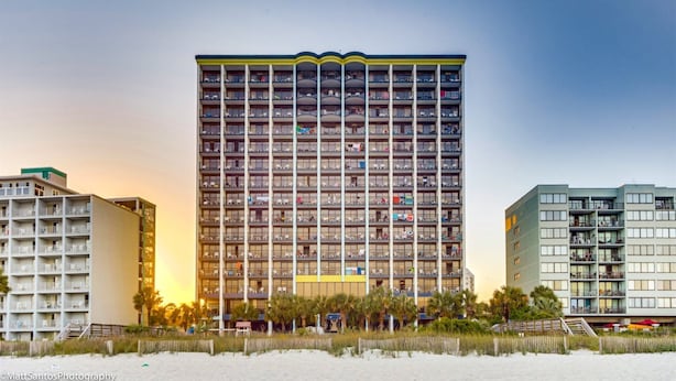 Hotel alto com várias varandas, situado perto de uma praia com areia na frente.