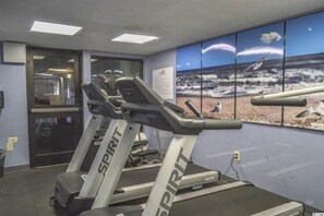 A gym with treadmills, a large wall mural of a beach scene, and a door leading to another room.