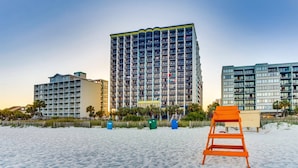 Um hotel à beira-mar com vários andares, varandas e uma praia arenosa em primeiro plano.