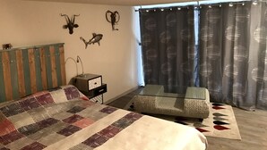 A bedroom with a bed, a small desk, a glass table, a sofa, and decorative wall art. - Appartement Mezzanine Avec Vue Exceptionnelle (Barcelonnette)