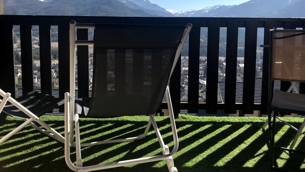 A balcony with a view of snow-capped mountains, a grassy area, and a chair. - Appartement Mezzanine Avec Vue Exceptionnelle (Barcelonnette)